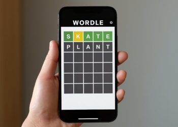 Hand holding a smartphone with Wordle game screen showing green and yellow tiles