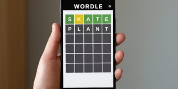 Hand holding a smartphone with Wordle game screen showing green and yellow tiles